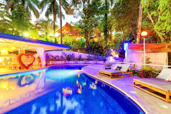 A swimming pool with lounge chairs and a covered seating area, surrounded by lush greenery and a building with a traditional roof. - ECOTICA Boutique Hotel & Spa. (Quepos)