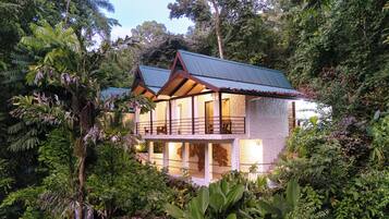Una casa de dos pisos rodeada de densa vegetación tropical.