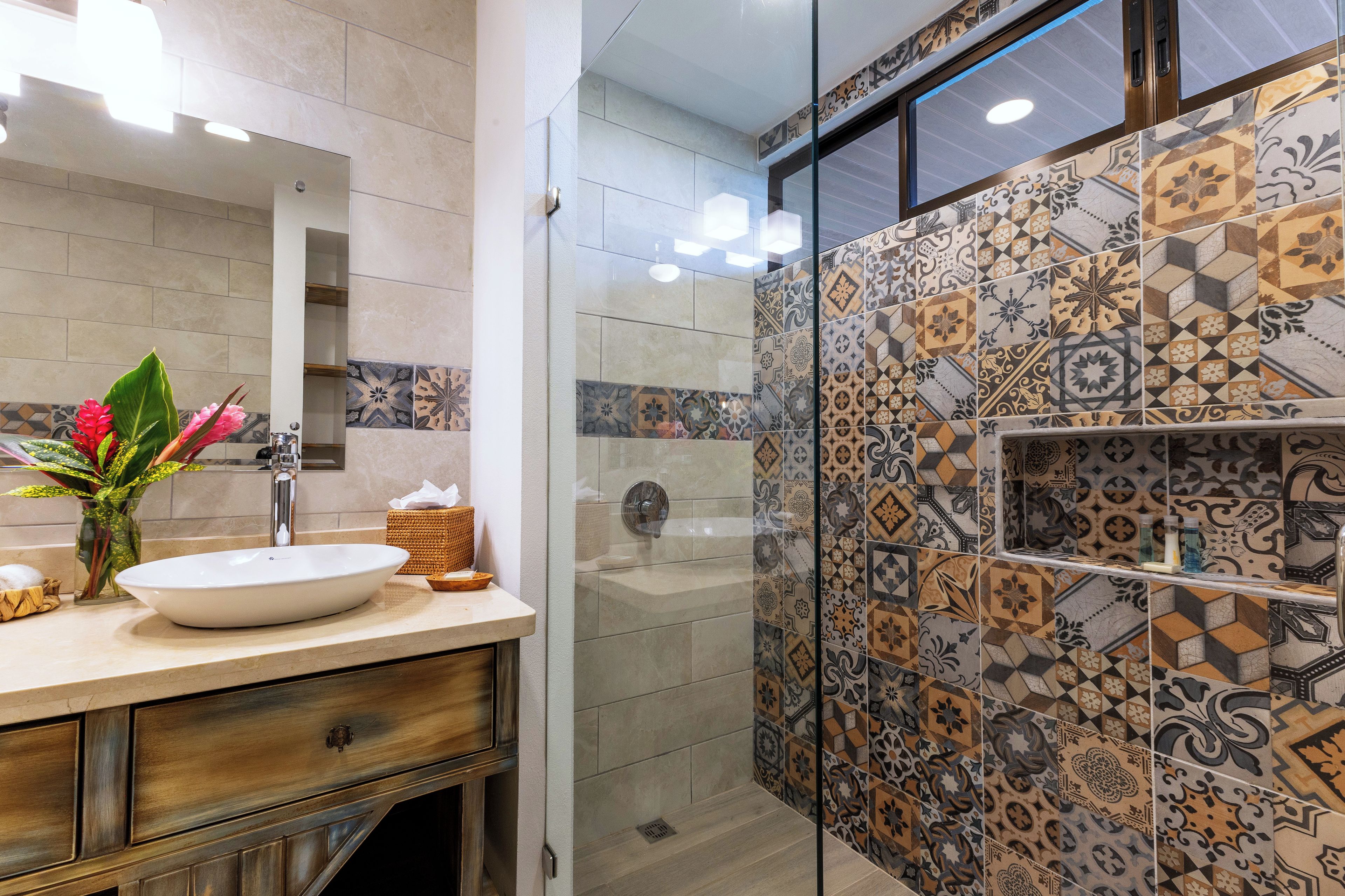 Un baño con un lavabo blanco, un espejo y una zona de ducha con azulejos estampados.