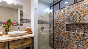 Un baño con un lavabo blanco, un espejo y una zona de ducha con azulejos estampados.