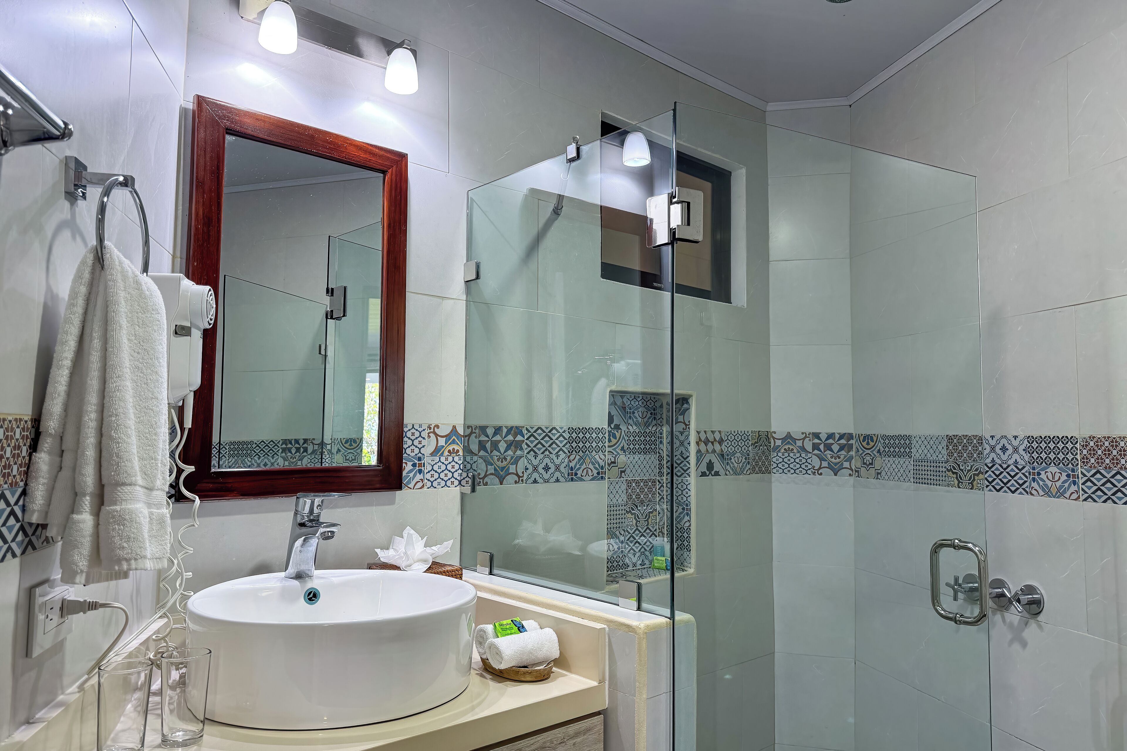 A modern bathroom with a large white sink, a glass shower enclosure, and a mirror with a wooden frame.