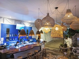 Zona de bar con un revoque de azulejos azules, lámparas colgantes de ratán y una barra con taburetes.