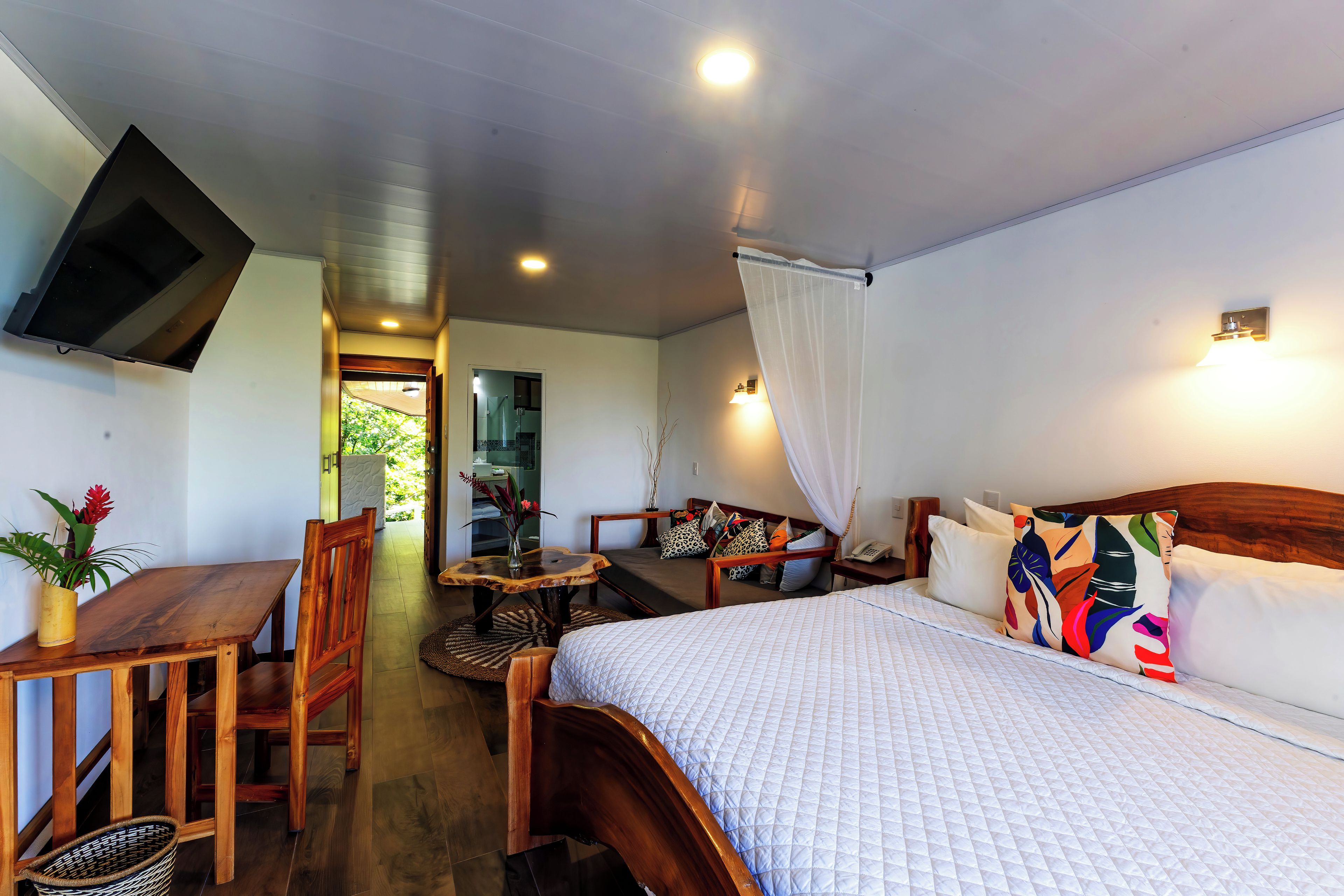 A hotel room with a bed, a desk, a chair, a television, and a bathroom visible through an open door.
