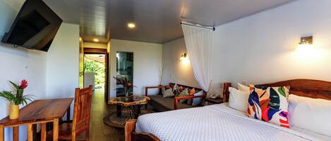 A hotel room with a bed, a desk, a chair, a television, and a bathroom visible through an open door.