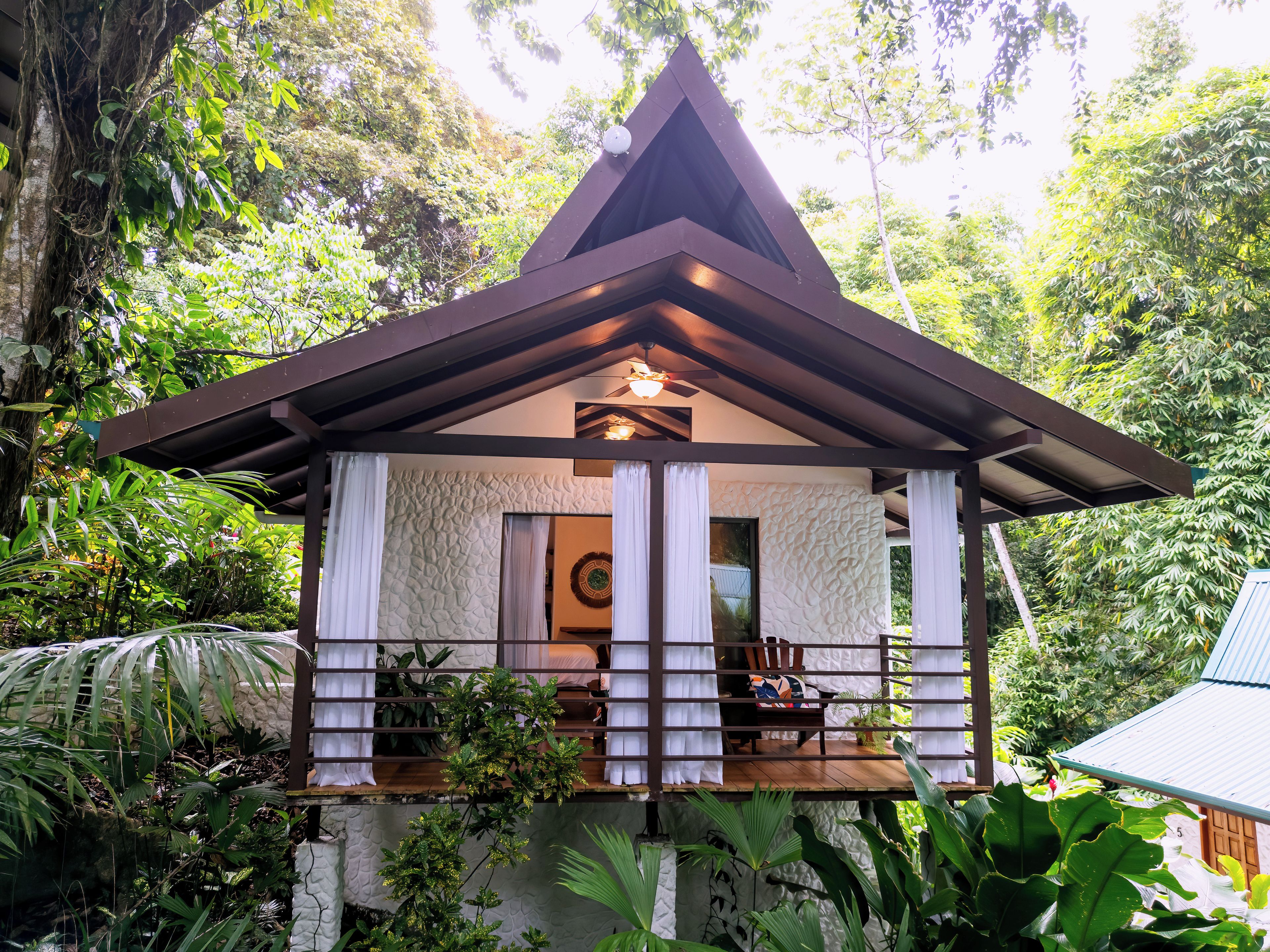 A small, single-story structure with a peaked roof, surrounded by lush greenery.