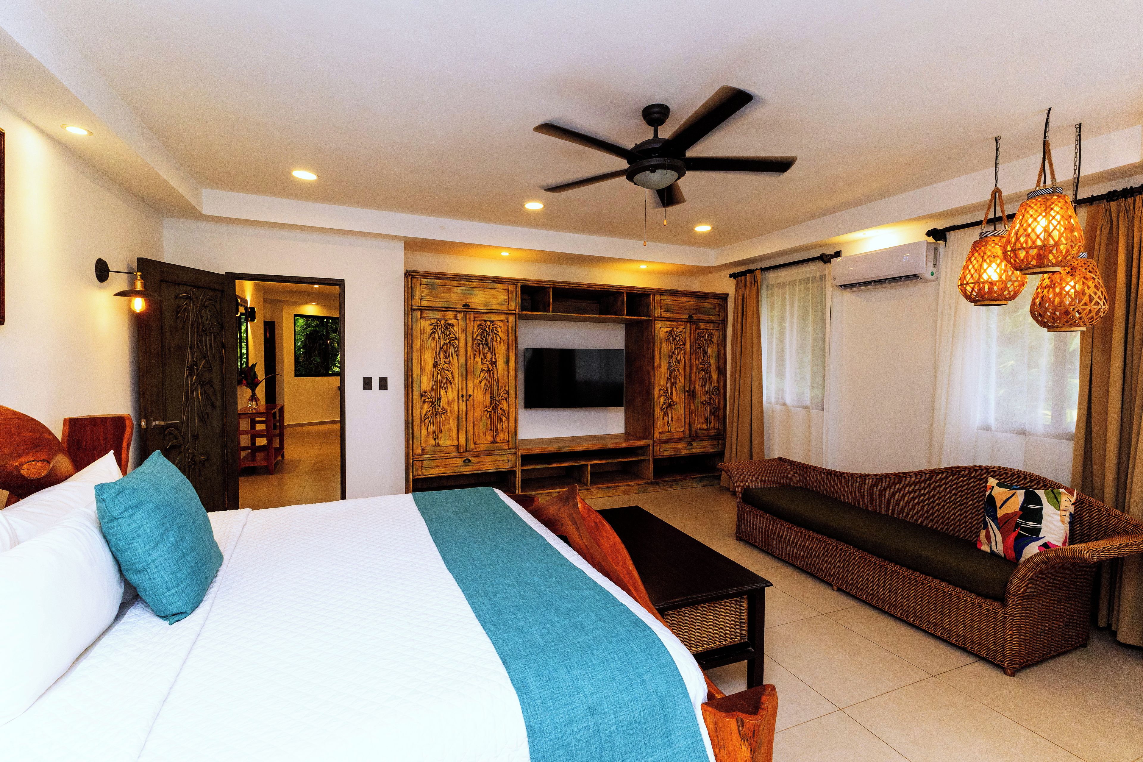 A hotel room with a large bed, a sofa, a TV, and a ceiling fan.