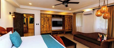 A hotel room with a large bed, a sofa, a TV, and a ceiling fan.