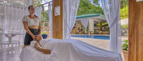 A spa area with a massage table, a person receiving a massage, and a pool in the background.
