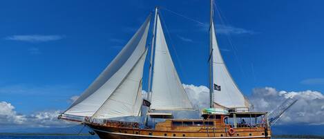 A large wooden sailing boat with multiple sails, a cabin, and a deck area with seating.