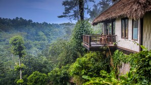 Un bungalow au toit de chaume doté d’un balcon donnant sur une forêt luxuriante.