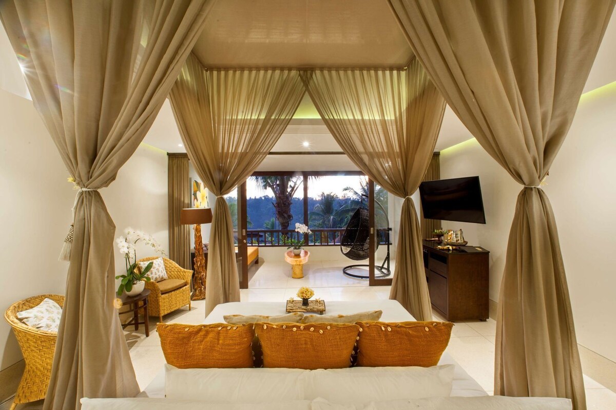Ein Schlafzimmer mit Bett, Vorhängen, Fernseher, Sofa, Lampe und Blick ins Freie.