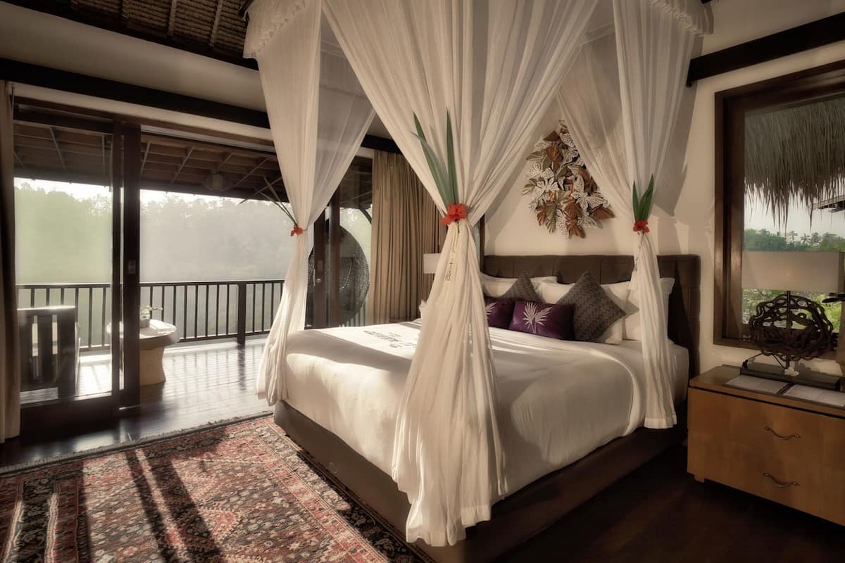 Een slaapkamer met een hemelbed, een nachtkastje, een groot raam en uitzicht op de omgeving.