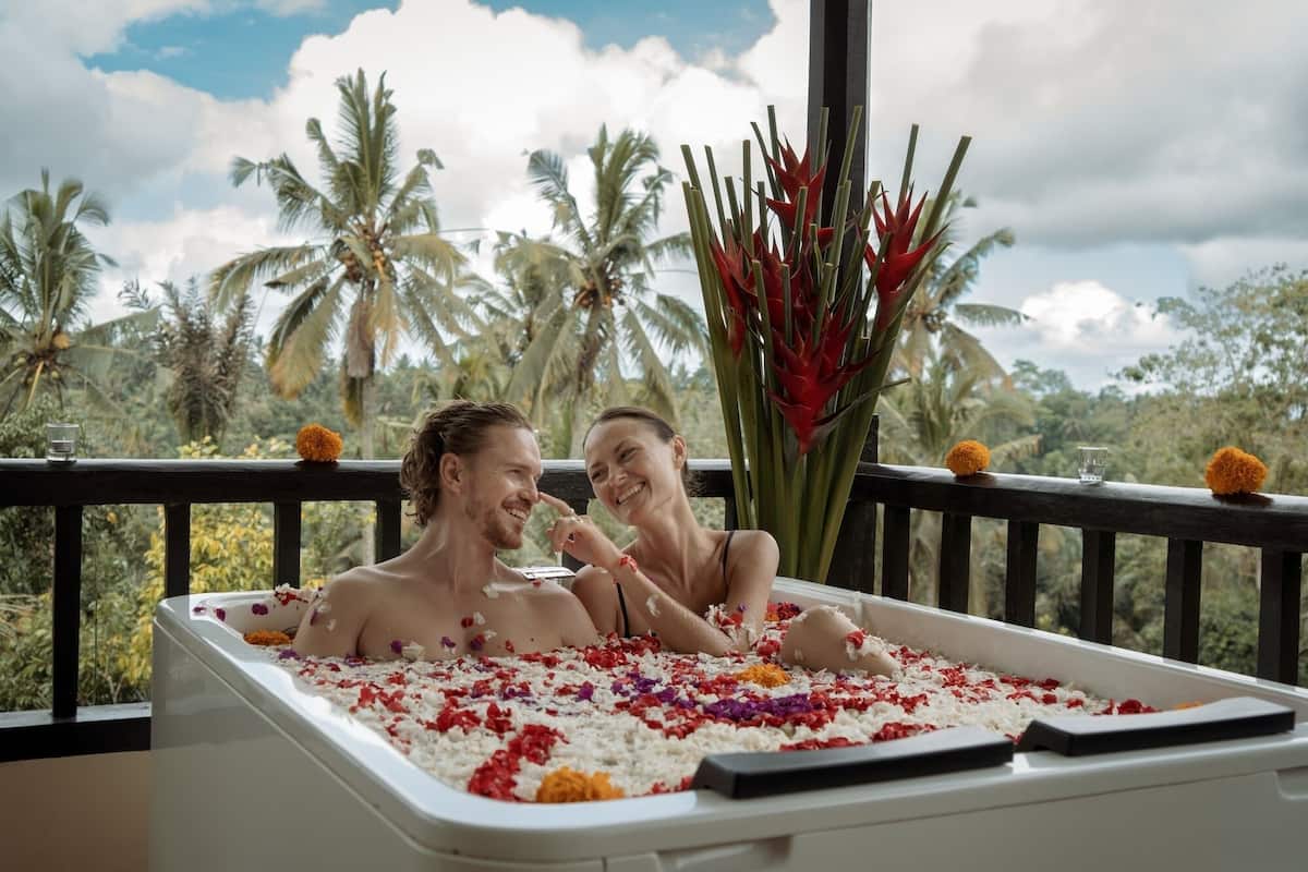 Een stel in een jacuzzi vol bloemblaadjes, omringd door tropische planten en palmbomen.