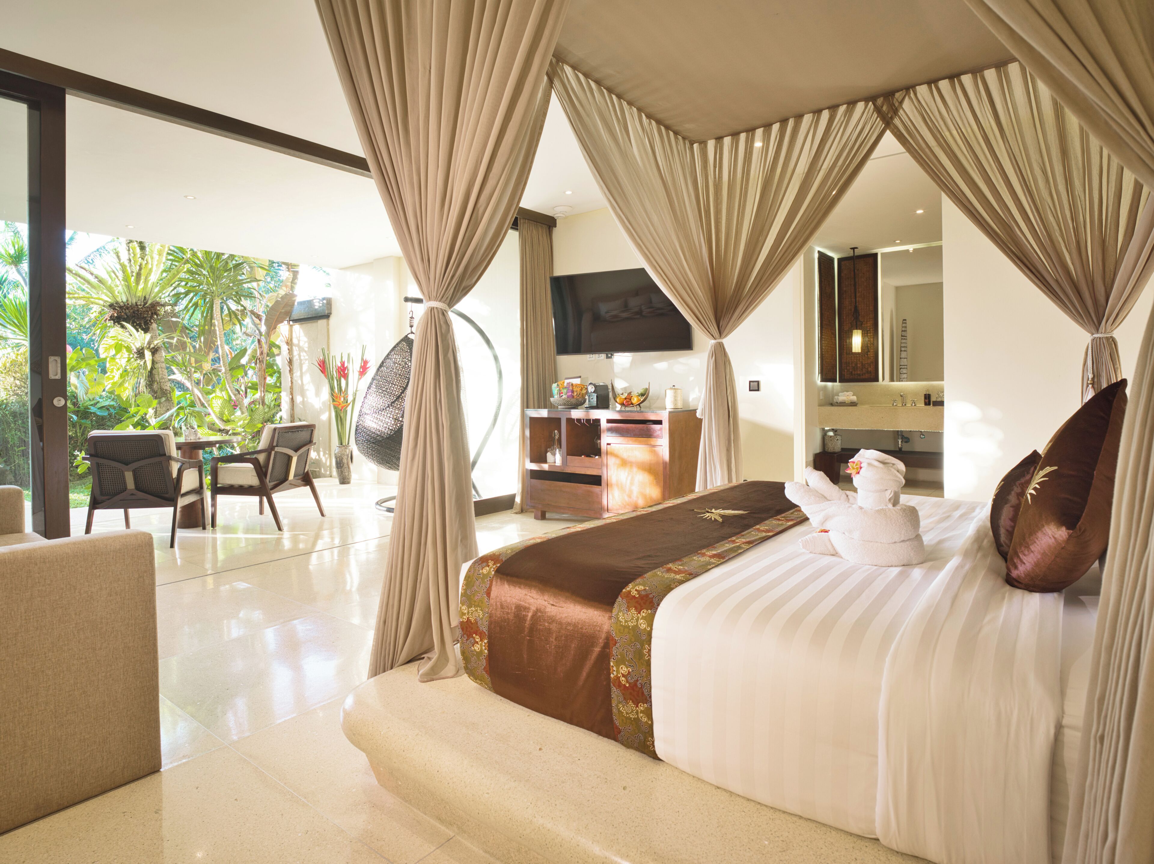 A spacious bedroom with a large bed, a sitting area with chairs, a desk, and a television.