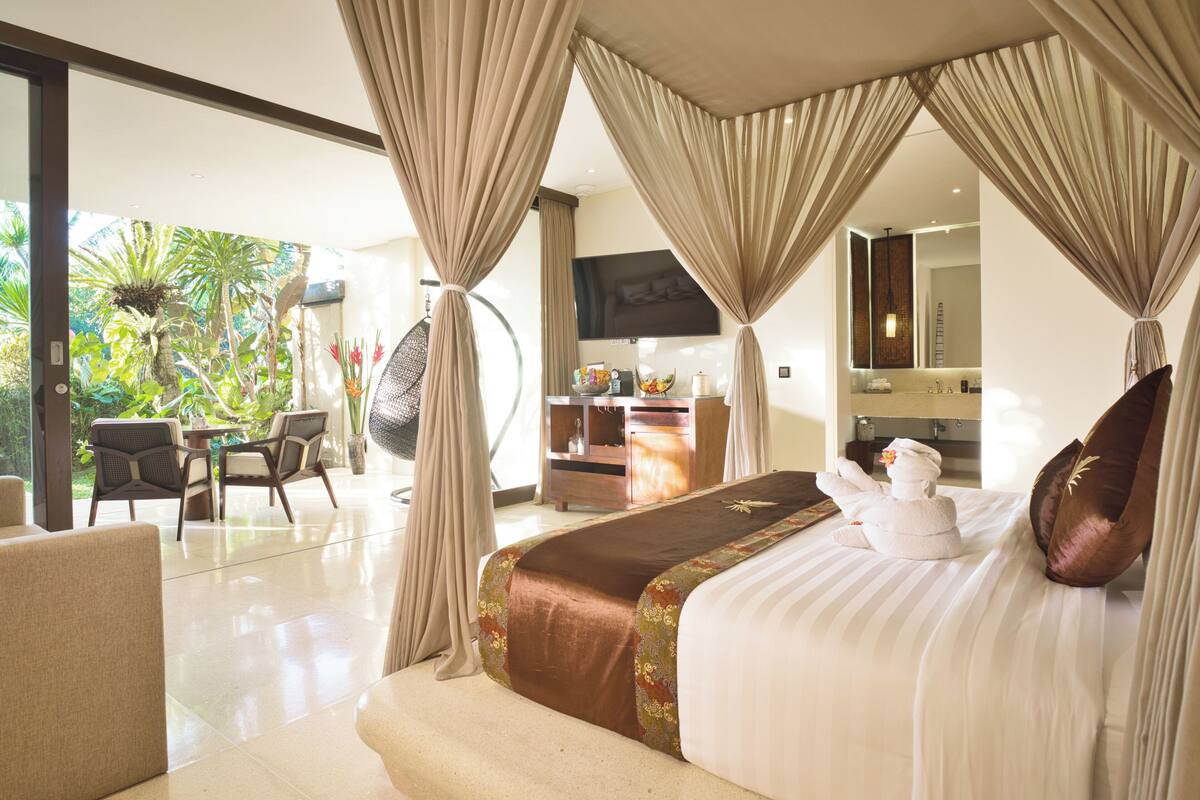 A spacious bedroom with a large bed, a sitting area with chairs, a desk, and a television.