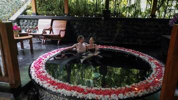 A circular hot tub surrounded by stone walls and a wooden deck with chairs.