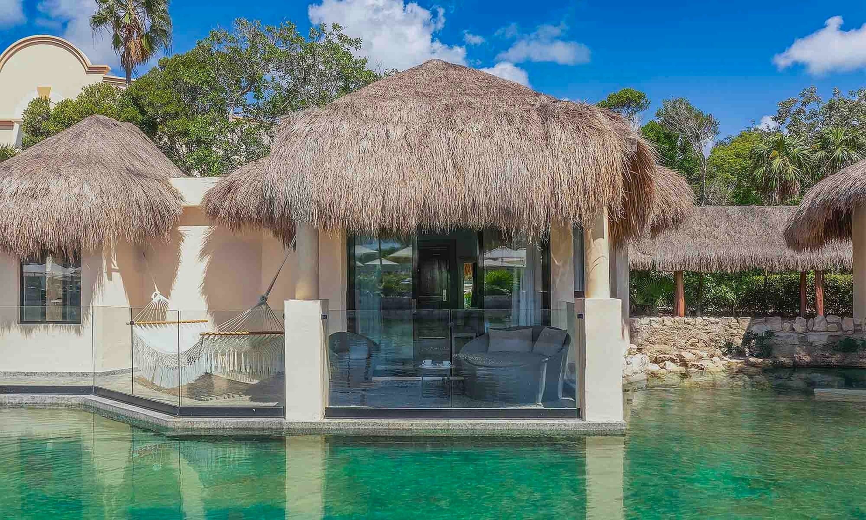 Un resort con bungalós sobre el agua con techo de paja, aguas cristalinas y exuberante vegetación.