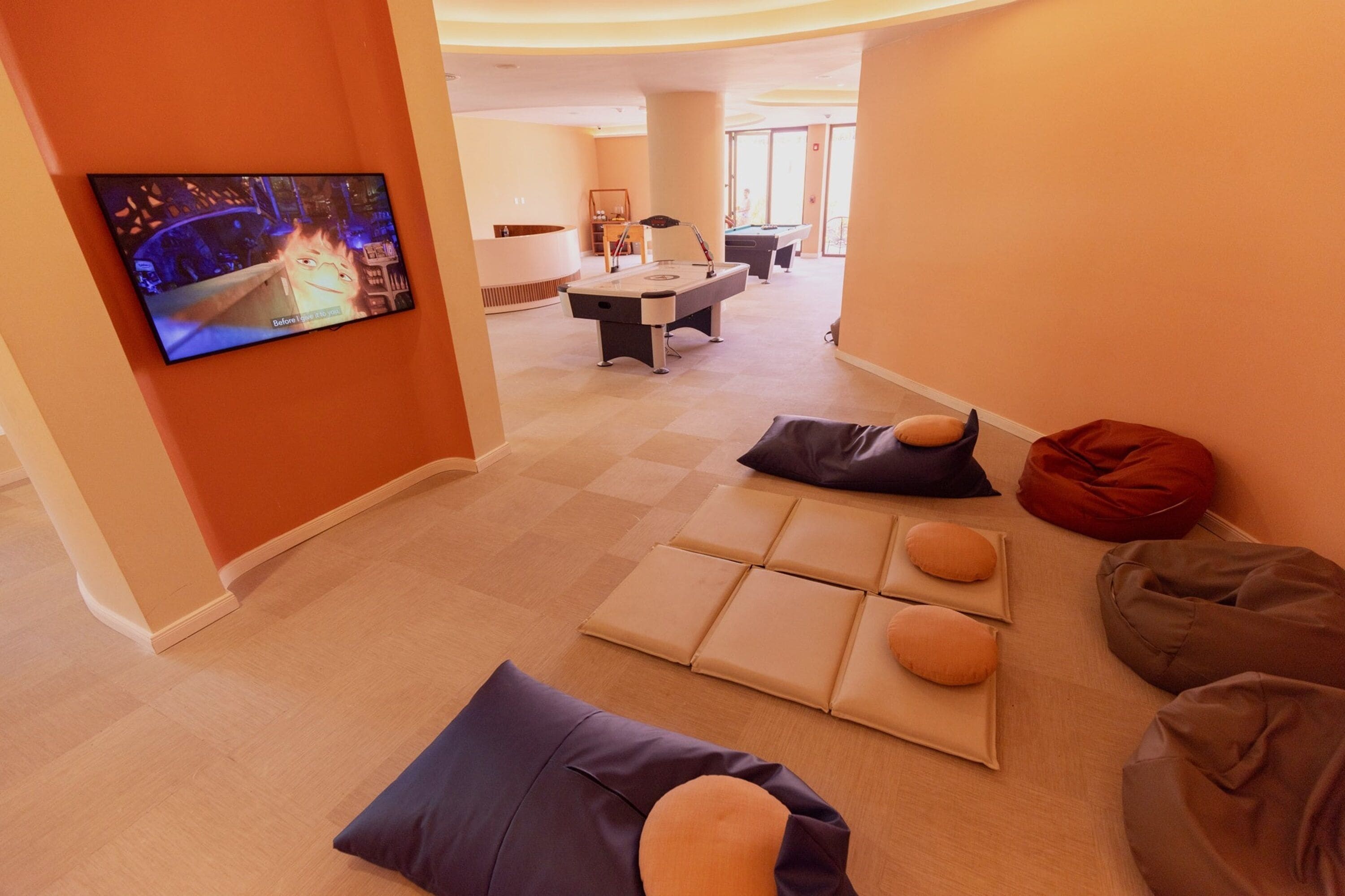 A modern living room with a flat-screen TV, a pool table, and a seating area with cushions.