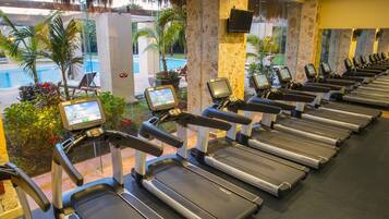 Una hilera de cintas de correr con pantallas digitales, una piscina y plantas de exterior.