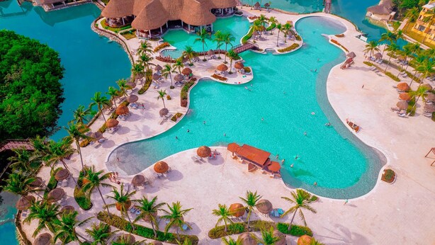 An aerial view of a resort with a large central pool, multiple smaller pools, and a beach area with umbrellas and lounge chairs. - Grand Palladium Select White Sand Resort & Spa - All Inclusive (Kantenah)