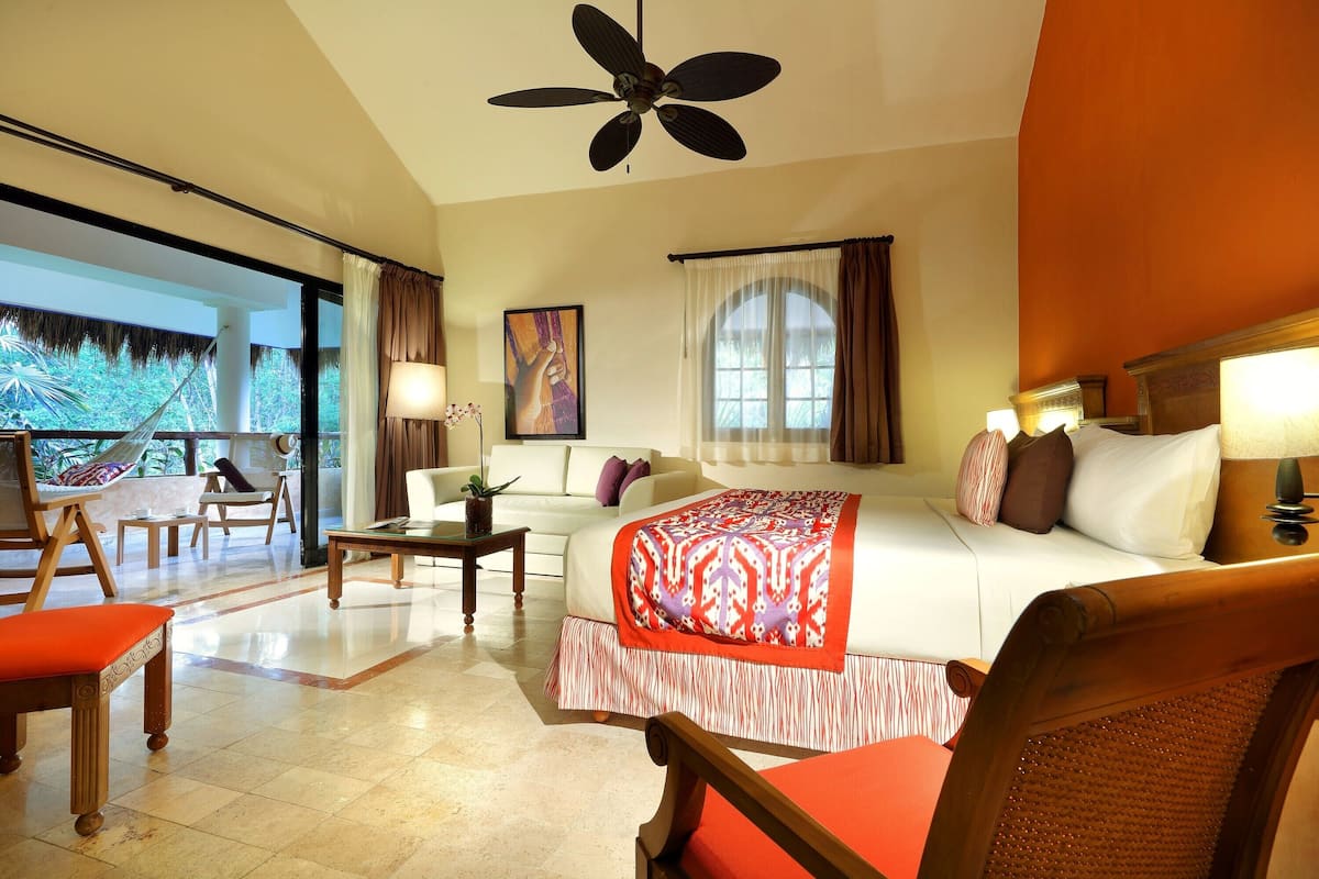A hotel room with a bed, a sofa, a chair, a small table, and a balcony with a hammock.