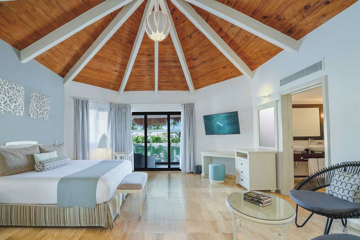 A bedroom with a wooden ceiling, a bed, a desk, a chair, and a TV.