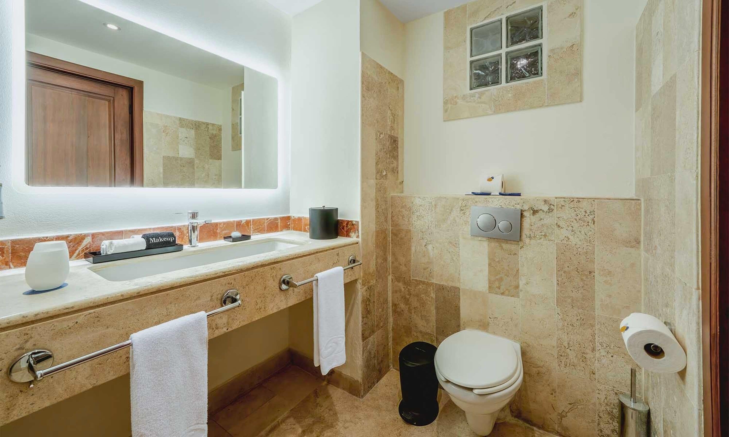 Un baño moderno con lavamanos de mármol, un espejo grande, inodoro y zona de ducha.