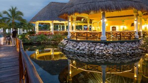 A thatched-roof outdoor dining area with a stone balustrade, reflecting on a calm water surface. - Grand Palladium Select White Sand Resort & Spa - All Inclusive (Kantenah)