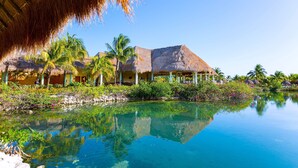 A resort with thatched-roof buildings, a clear pool, and lush greenery. - Grand Palladium Select White Sand Resort & Spa - All Inclusive (Kantenah)