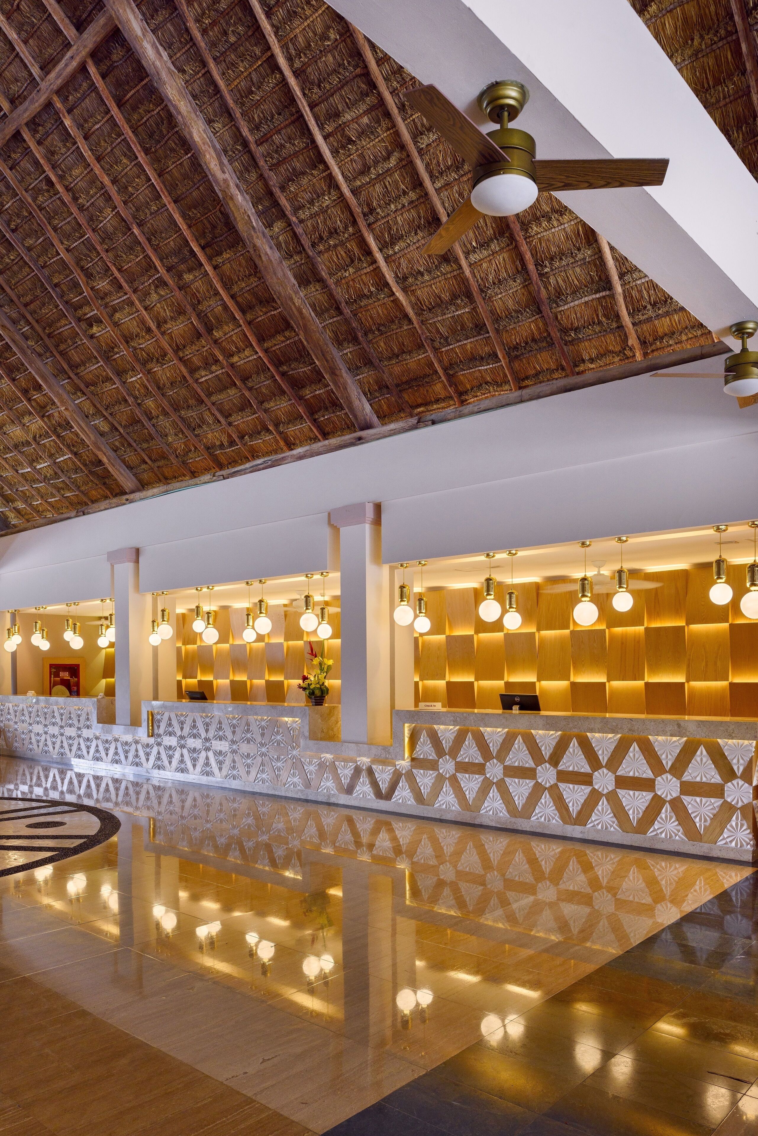 A reception area with a high ceiling, a thatched roof, and a reception desk with a patterned barrier.