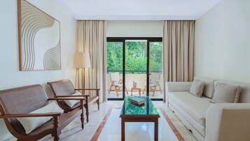 A modern living room with a sofa, two armchairs, a glass coffee table, and a large window with curtains.