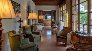 Un salón espacioso con sillones verdes, una mesa de centro y una chimenea. Amplias ventanas ofrecen vistas al exterior.