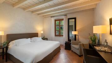 Habitación de hotel con una cama grande, un escritorio con silla, una mesita y una ventana con cortinas.