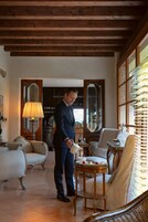 Un hombre con traje de pie en una habitación con techo de madera, una zona de bar al fondo y una mesa de comedor con un bol y fresas.