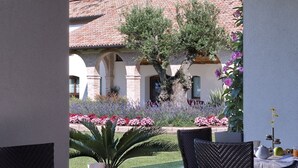 An outdoor dining area with a table set for breakfast, including fruits and beverages, overlooking a building with a tiled roof and garden. - Annia Park Hotel Venice Airport (Mestre)