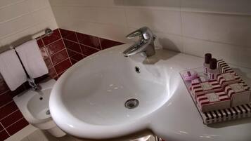 Ein Badezimmer mit einem weißen Waschbecken, einem Bidet und einem Spiegel. Auf dem Waschbecken liegen Toilettenartikel.