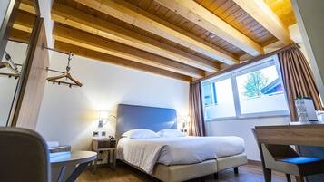 Habitación de hotel con techo de madera, cama con ropa de cama blanca, escritorio con silla y ventana con cortinas.
