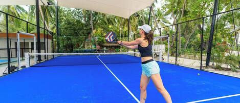 A tennis court with a net, surrounded by a fence and palm trees.
