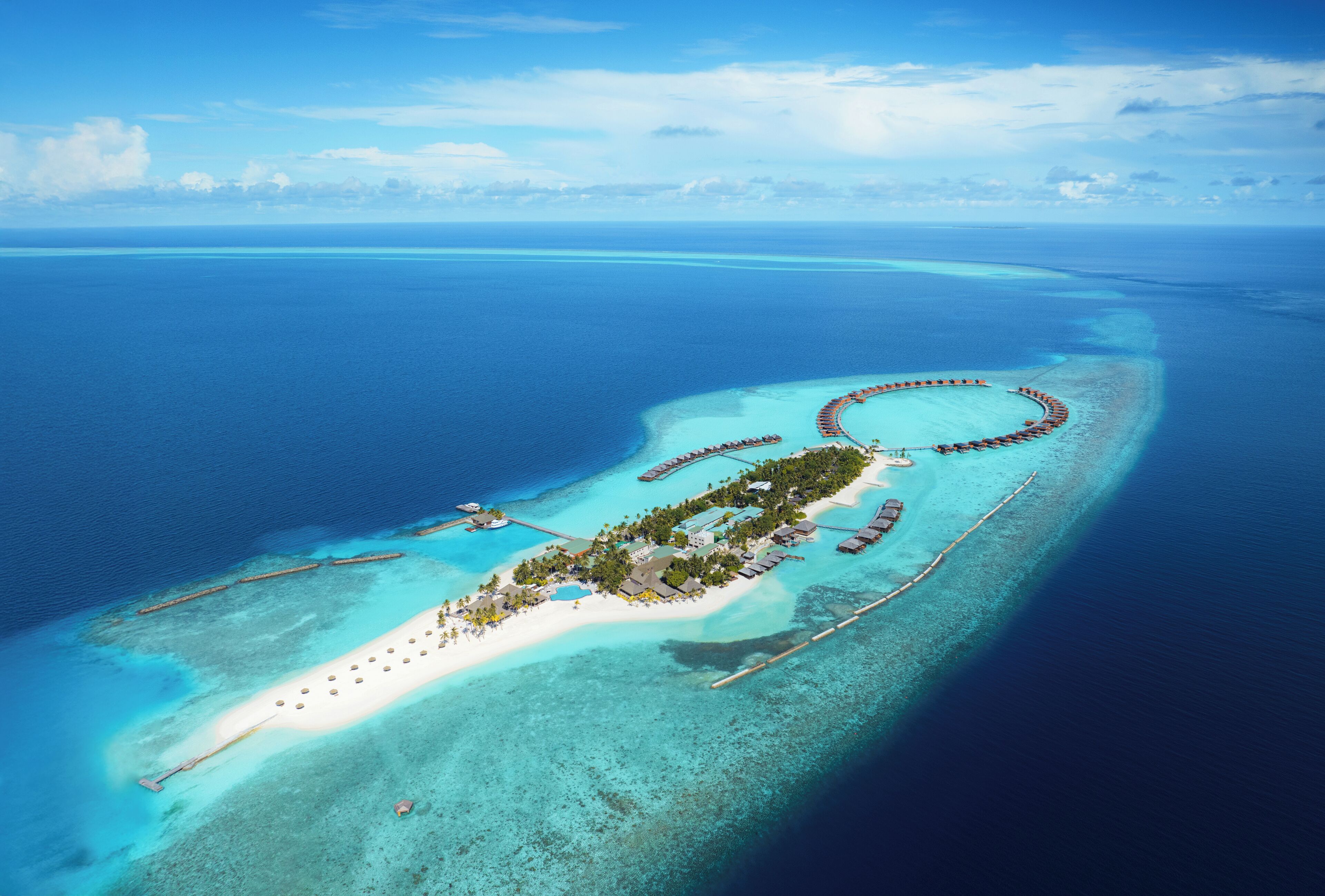 An aerial view of a resort island with overwater bungalows, a central building, and a beach.