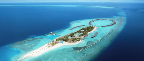 An aerial view of a resort island with overwater bungalows, a central building, and a beach.
