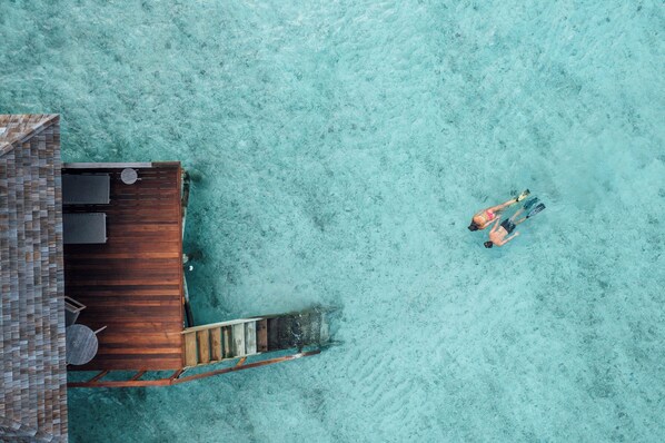 A wooden deck extending into clear turquoise water, with a small boat docked nearby. - Veligandu Maldives Resort Island (Veligandu Island)