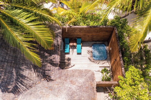 Vista aérea de una terraza de madera con dos sillones de descanso y una pequeña piscina, rodeada de exuberante follaje y palmeras.