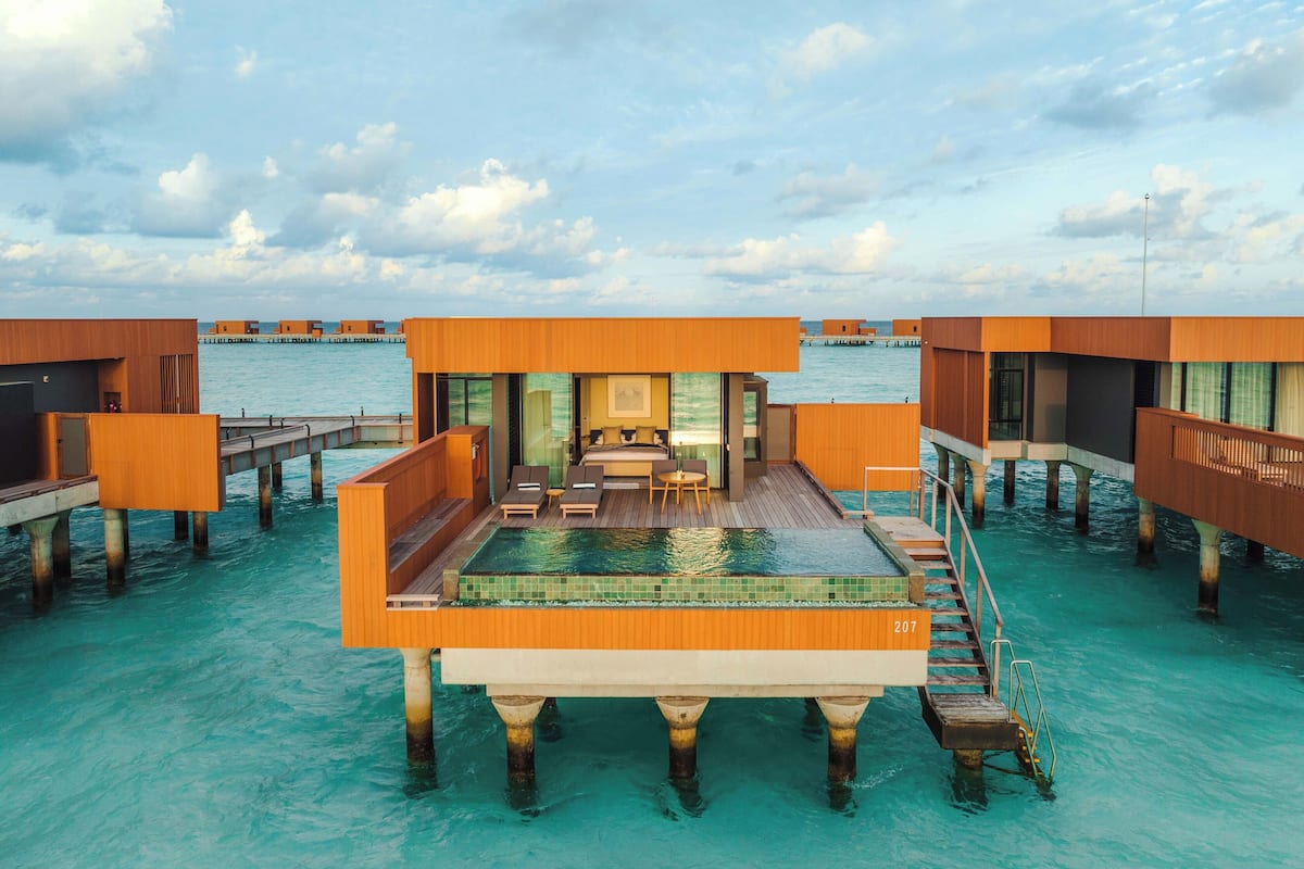 Una cabaña sobre el agua con piscina, terraza de madera y vistas al océano.