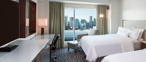 Habitación de hotel con dos camas, un escritorio, una silla y vistas a la silueta de la ciudad.