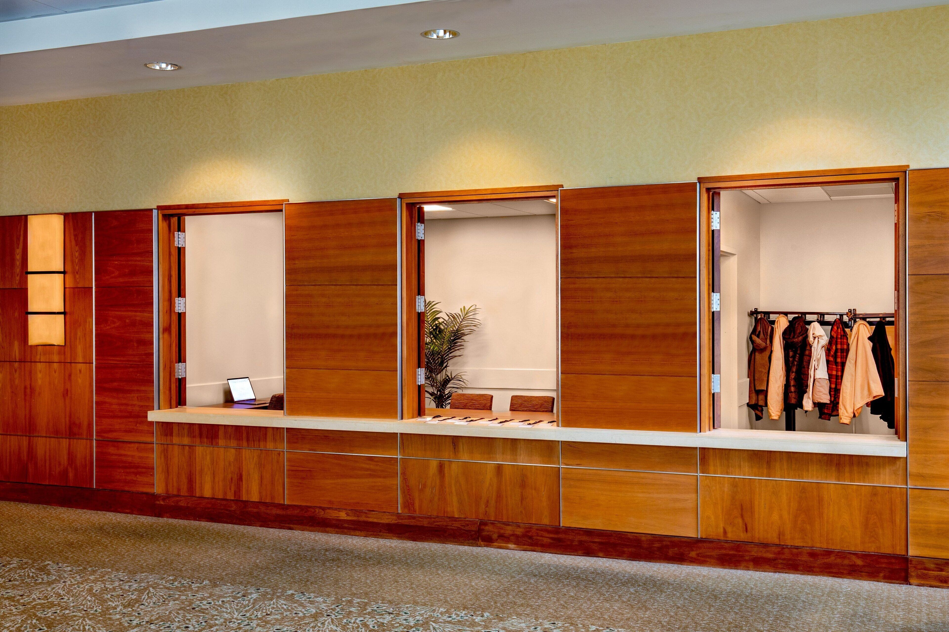 A hotel reception area with a wooden reception desk, a laptop, and a clothing rack.