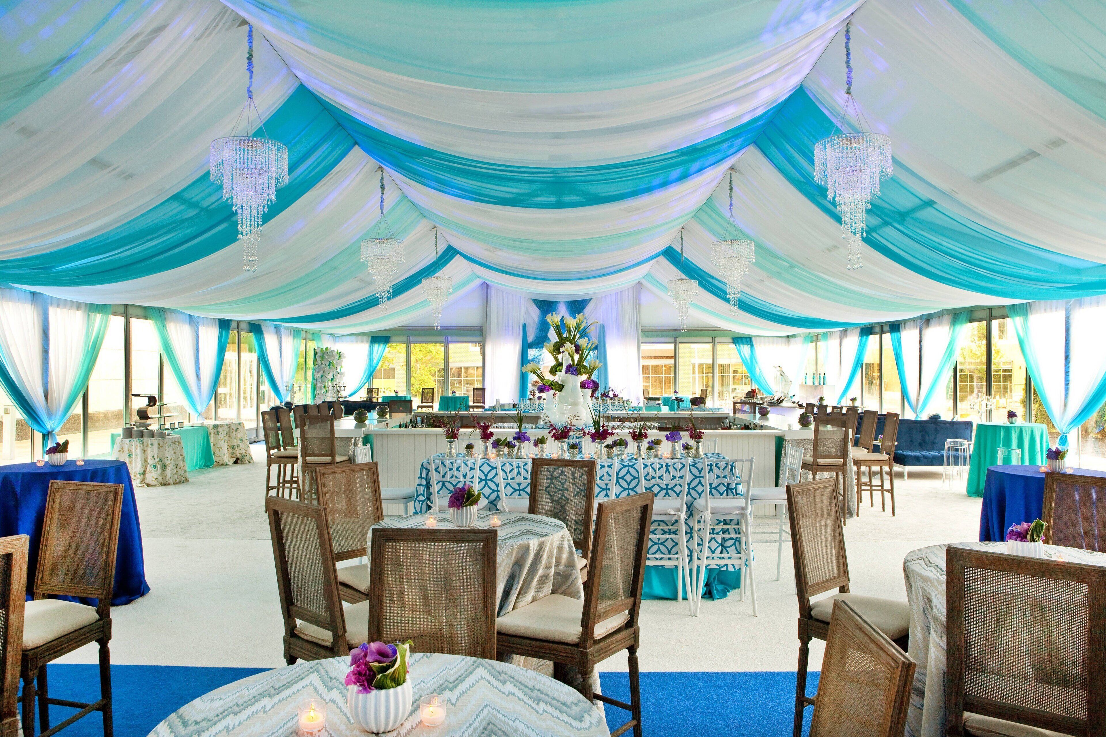 A tented event space with tables and chairs, draped in blue and white fabric, and chandeliers hanging from the ceiling.