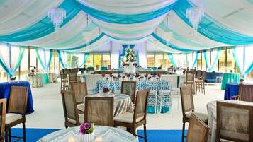 A tented event space with tables and chairs, draped in blue and white fabric, and chandeliers hanging from the ceiling.