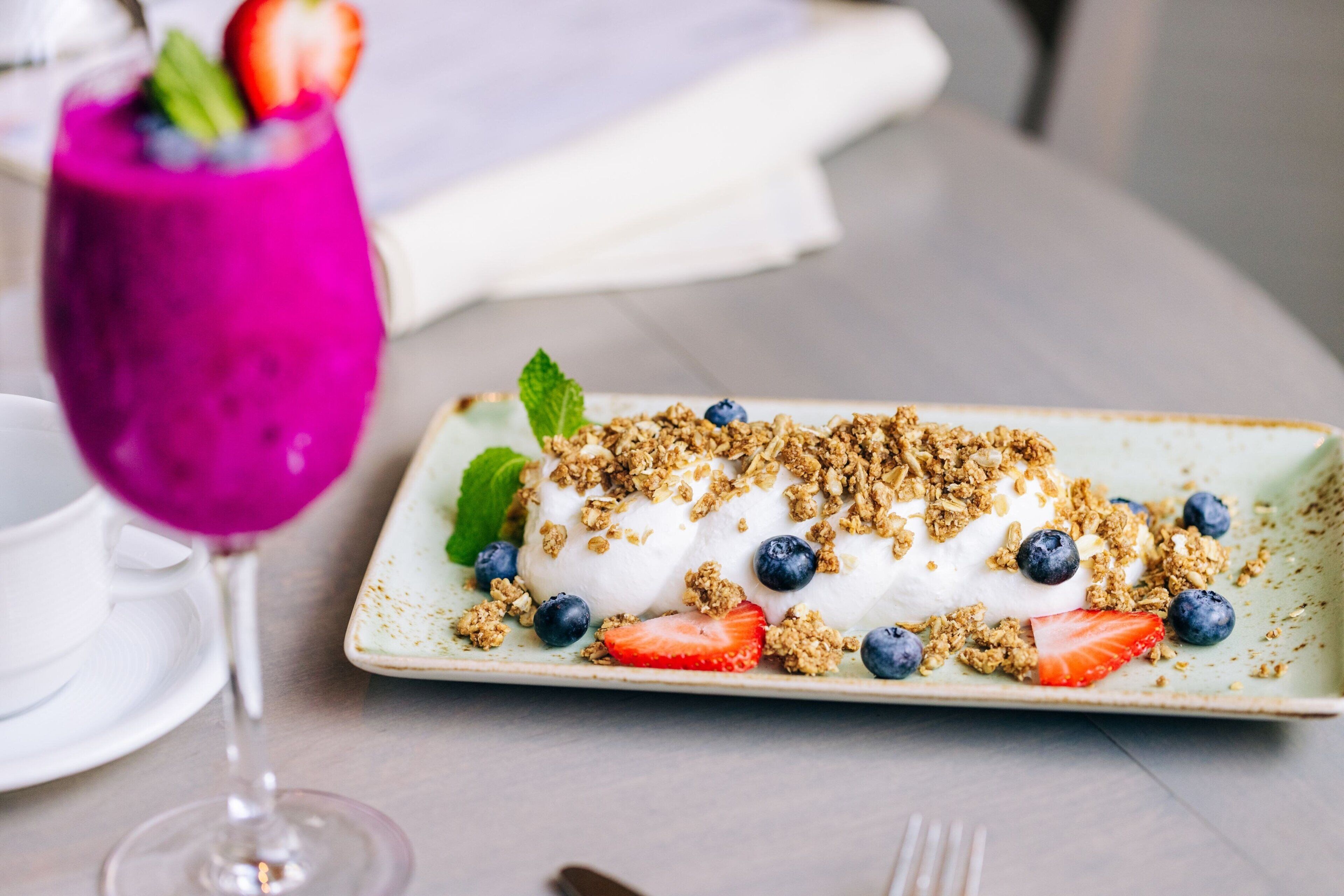 A dessert plate with yogurt, granola, strawberries, and blueberries on a ceramic plate.