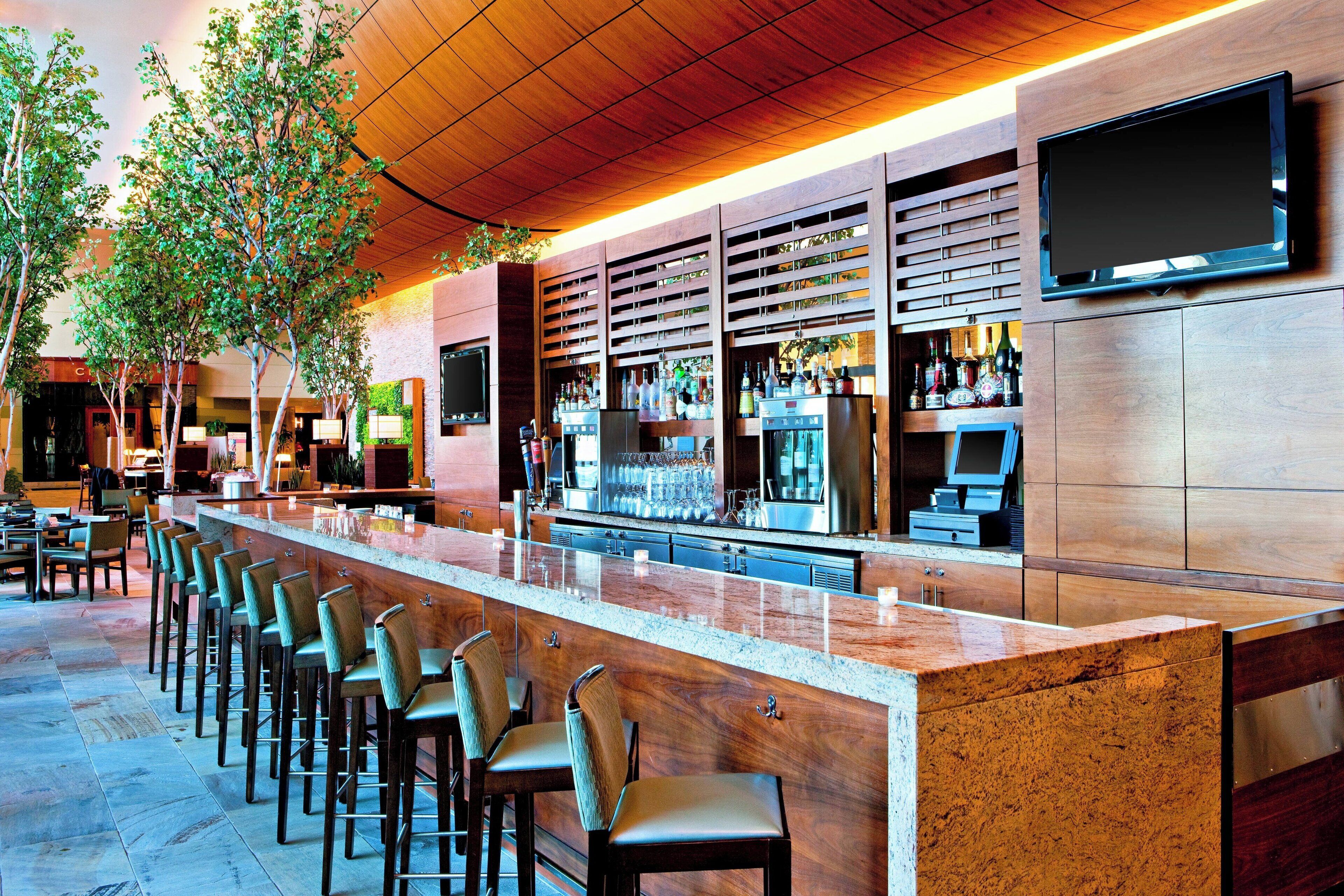 A bar area with a long counter, multiple stools, and a television mounted on the wall.
