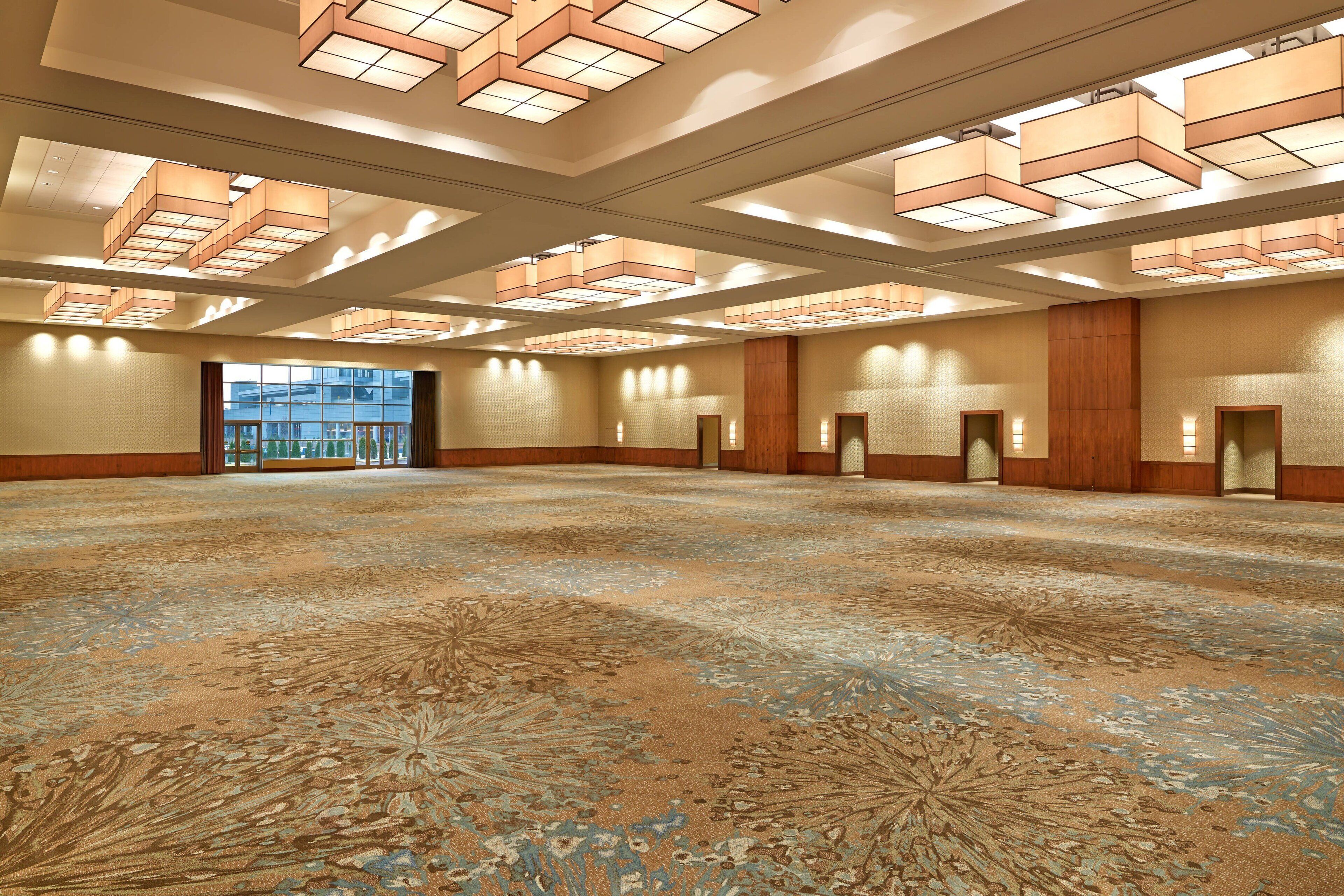 A spacious hotel lobby with a patterned carpet, recessed lighting, and a large glass entrance.